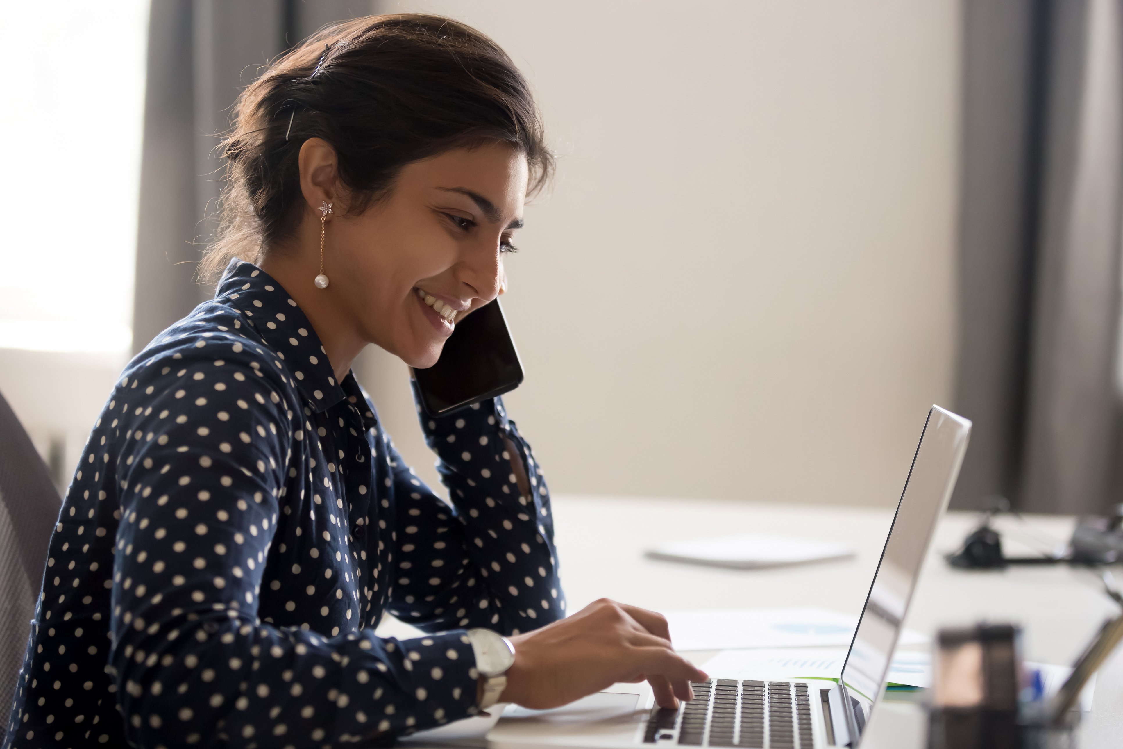 Smiling-employee-working-on-laptop-talking-over-phone-1172966600_3869x2579